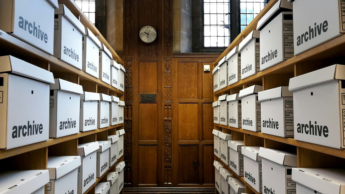 Des rangées de boîtes d'archives blanches sur des étagères en bois, illustrant l'organisation et le stockage de l'information