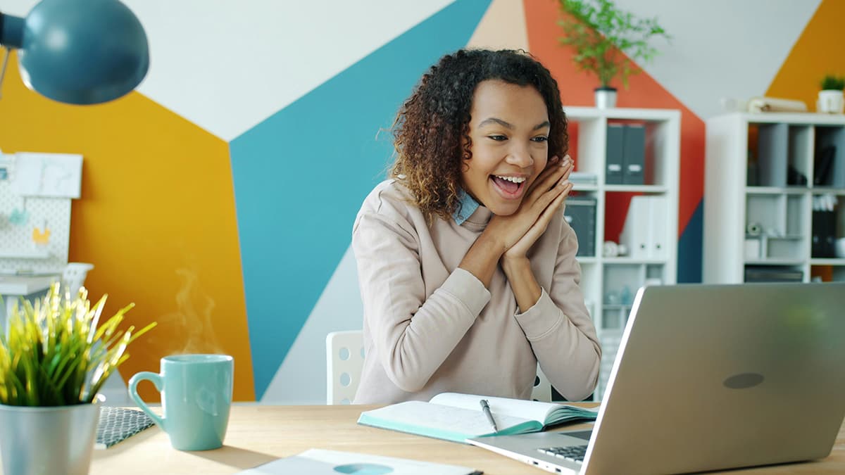 Une femme enthousiaste devant son ordinateur portable, illustrant le moment de révélation (Aha! moment) d'un prospect