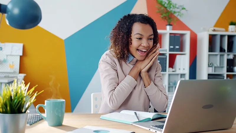 Une femme enthousiaste devant son ordinateur portable, illustrant le moment de révélation (Aha! moment) d'un prospect