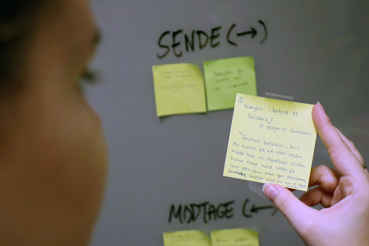 Une personne structurant une réflexion avec un post-it devant un tableau blanc