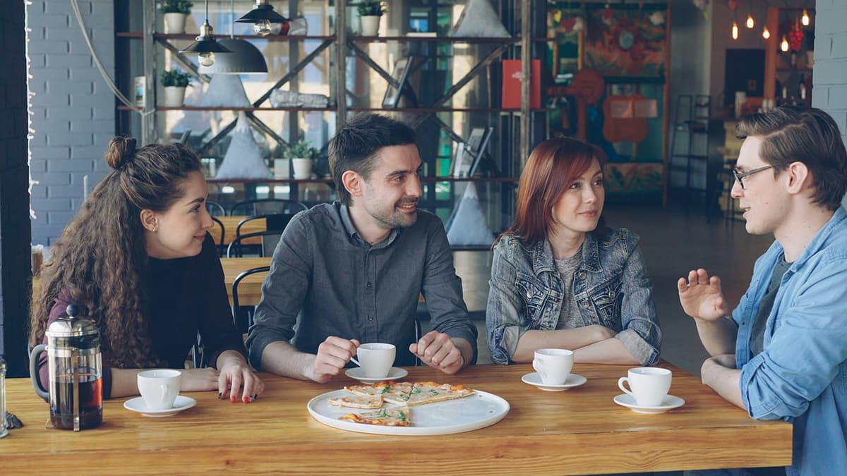 Un groupe d'amis discutant et riant joyeusement autour d'un café, illustrant la conversation et le réseautage authentique