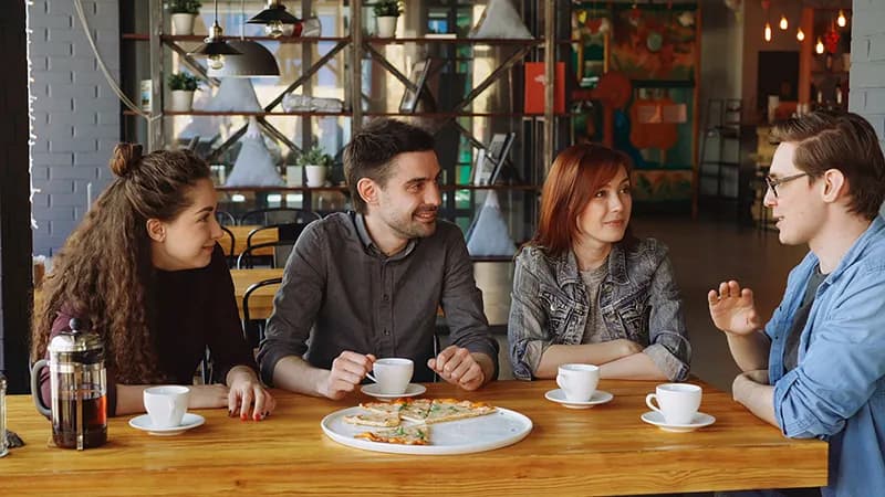 Un groupe d'amis discutant et riant joyeusement autour d'un café, illustrant la conversation et le réseautage authentique