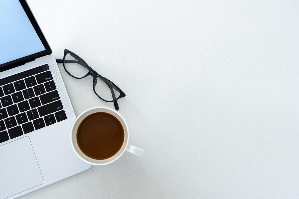 Un bureau organisé avec un ordinateur portable, des lunettes et un café, symbolisant la productivité