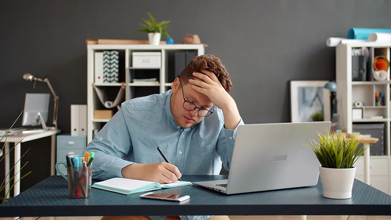 Un homme stressé devant son ordinateur, illustrant le burn-out et la surcharge de travail en période de rush client