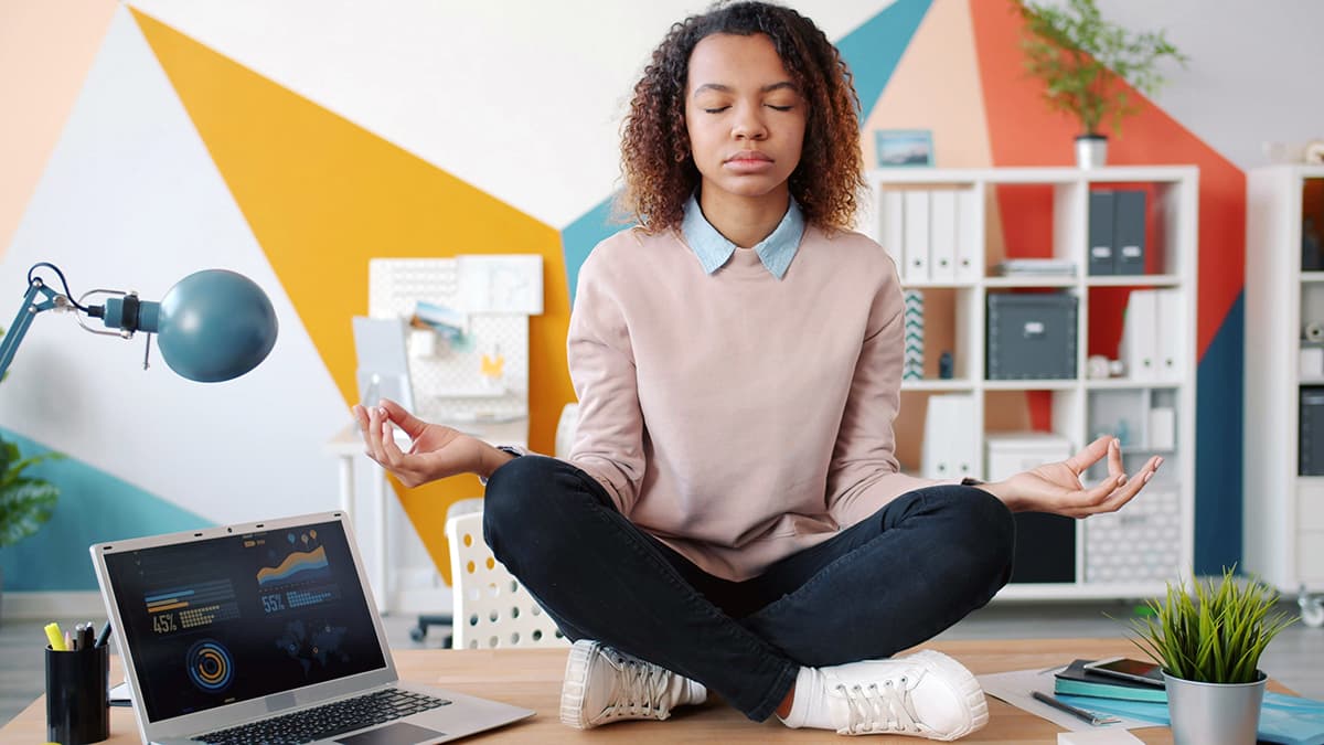Une femme méditant à son bureau devant son ordinateur portable pour retrouver son calme