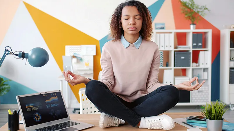 Une femme méditant à son bureau devant son ordinateur portable pour retrouver son calme