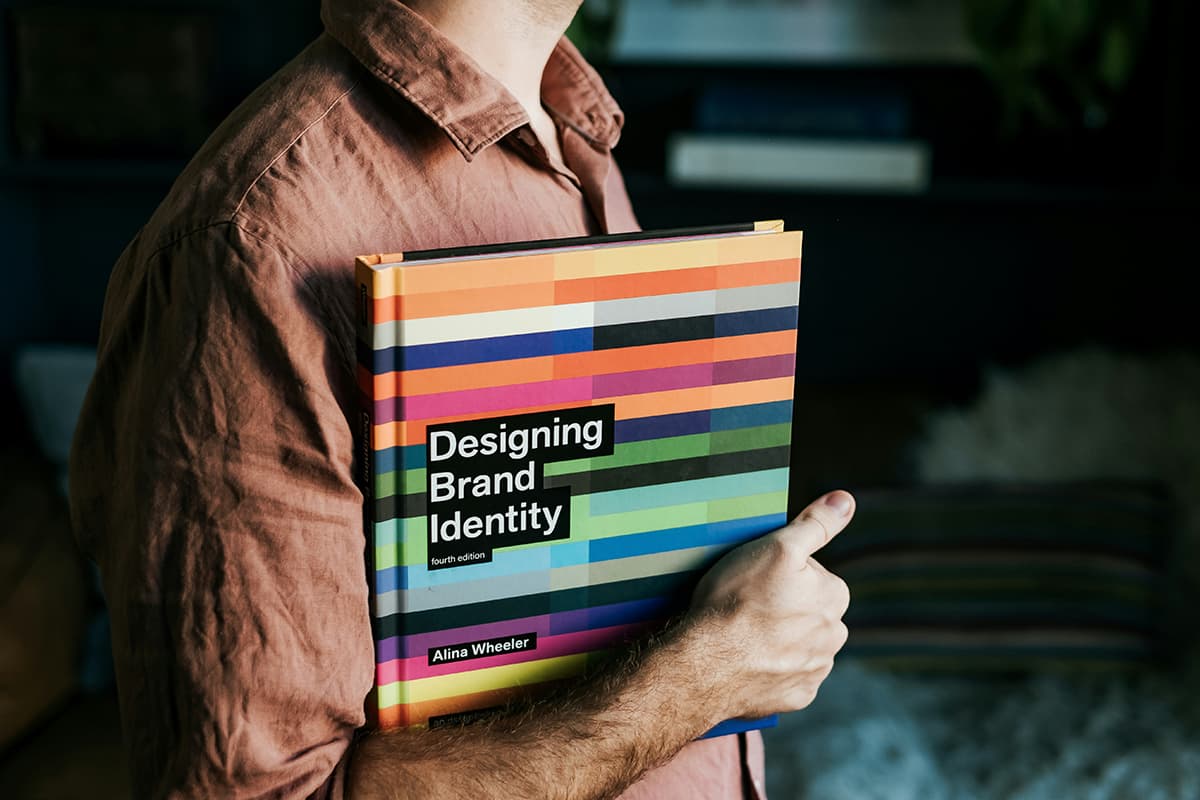 Un homme tenant un livre intitulé 'Designing Brand Identity', symbolisant la construction d'une marque forte