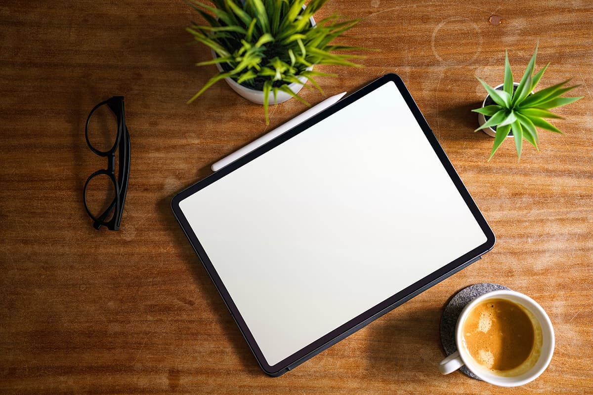 Une tablette affichant un document posée sur un bureau en bois à côté d'un café