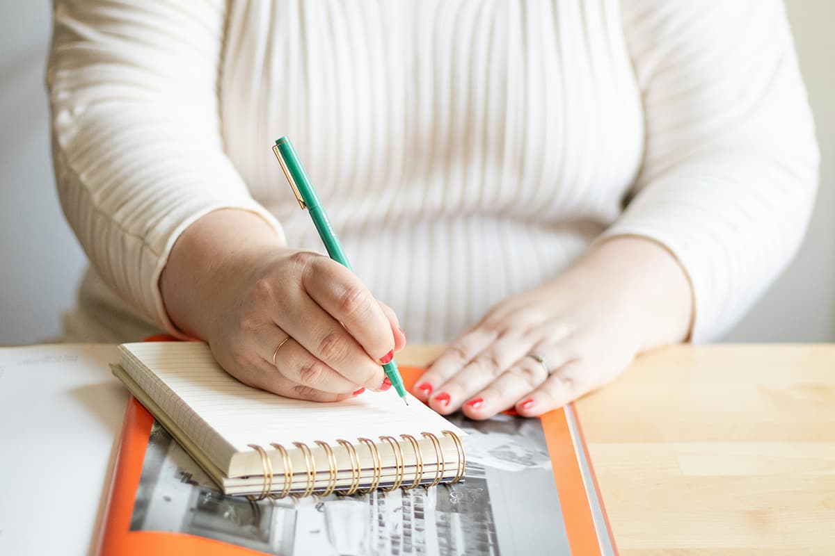 Gros plan sur une personne absorbée par l'écriture dans un carnet, symbolisant le processus créatif structuré et le focus