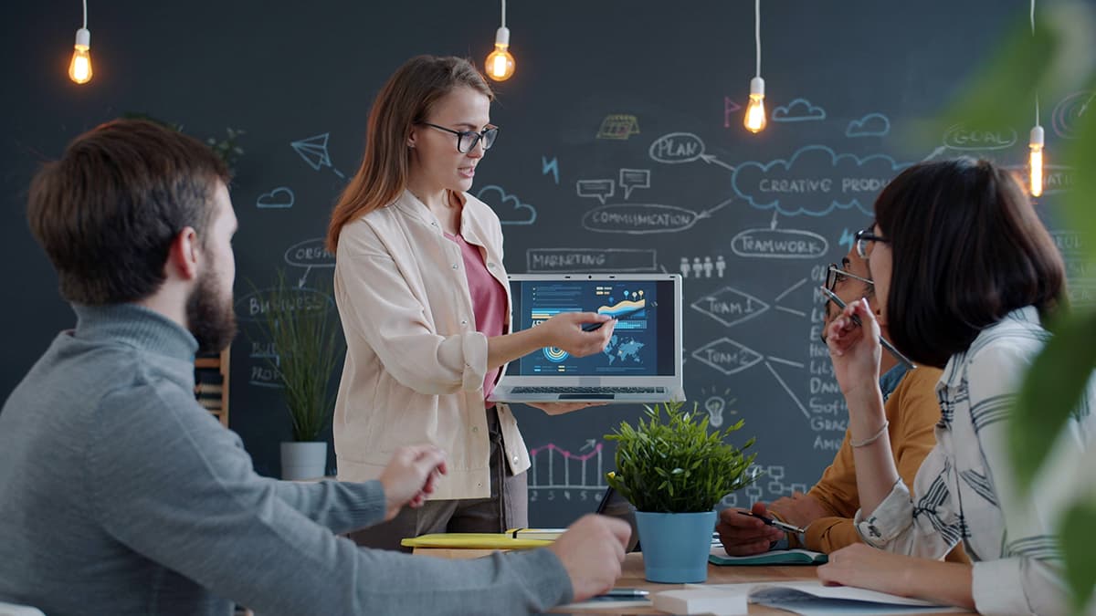 Une experte présentant une stratégie d'entreprise sur un écran à ses collaborateurs, symbolisant la transmission pédagogique et l'autorité