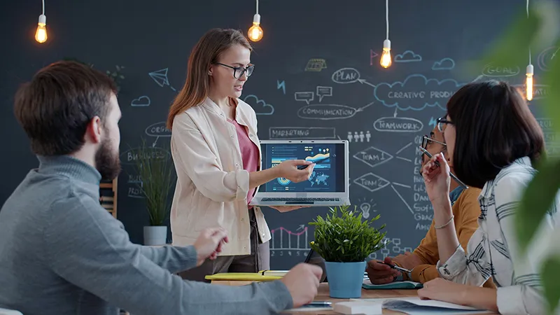 Une experte présentant une stratégie d'entreprise sur un écran à ses collaborateurs, symbolisant la transmission pédagogique et l'autorité