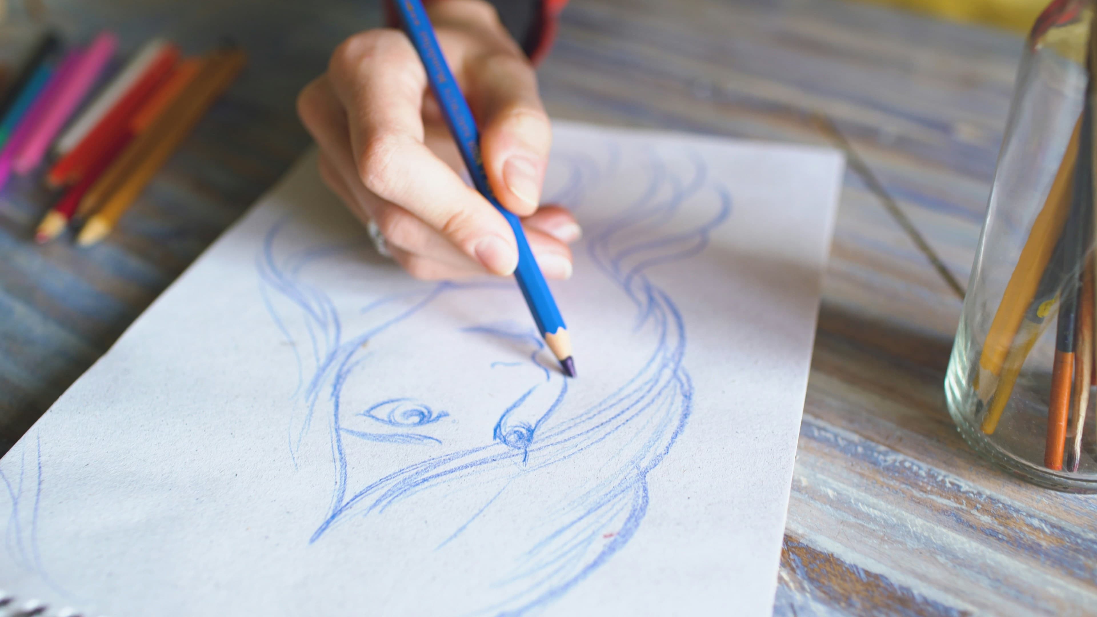 Gros plan sur une main dessinant un croquis au crayon bleu dans un carnet, symbolisant l'inspiration