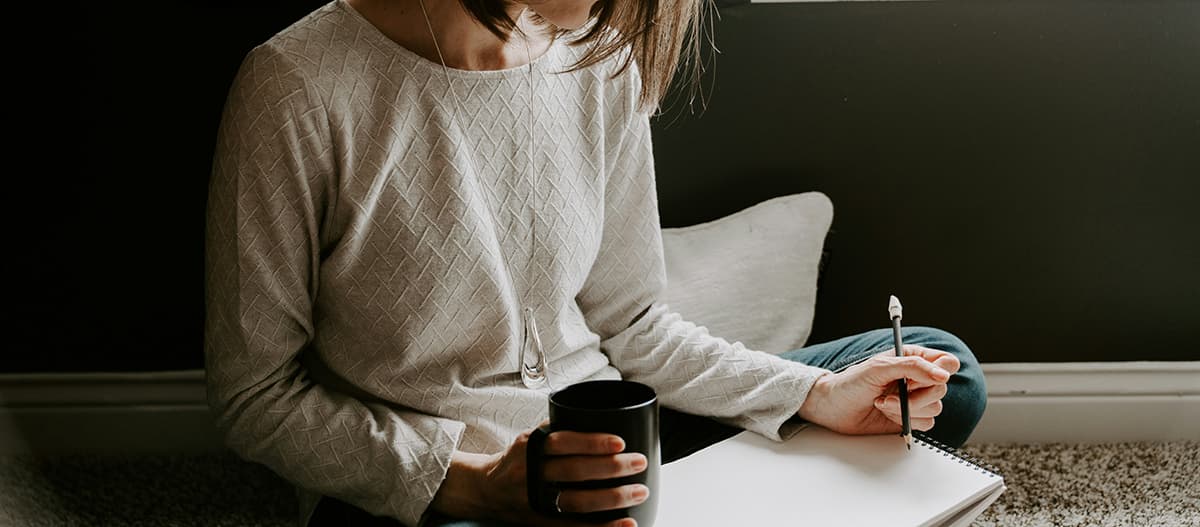 Une personne écrivant au calme dans un carnet avec une tasse de café, symbolisant le retour au calme et la créativité