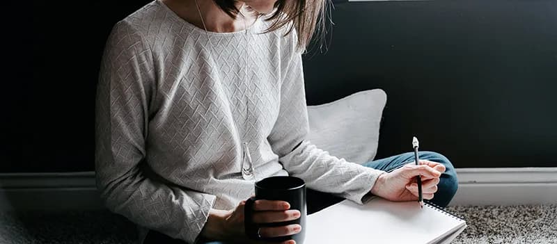 Une personne écrivant au calme dans un carnet avec une tasse de café, symbolisant le retour au calme et la créativité