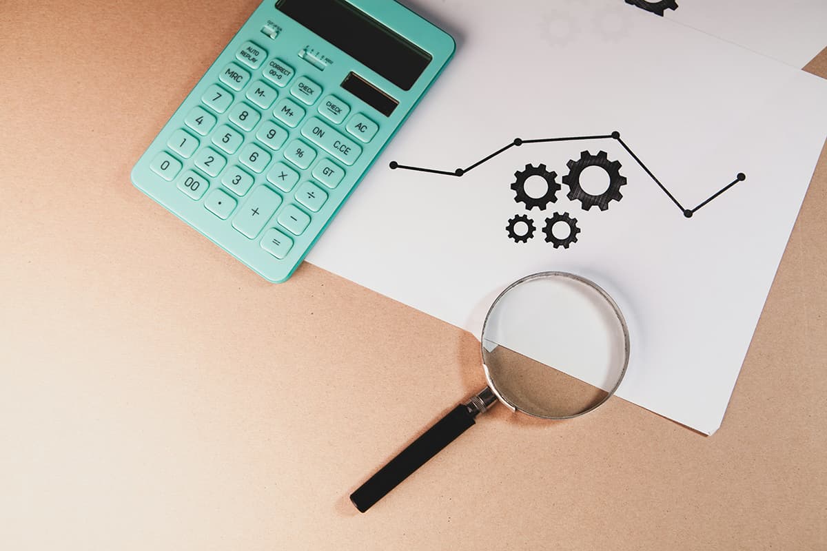 Une loupe, des graphiques financiers et une calculatrice sur un bureau, illustrant la déconstruction minutieuse des concurrents