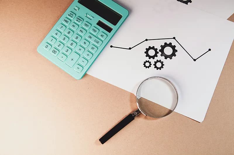 Une loupe, des graphiques financiers et une calculatrice sur un bureau, illustrant la déconstruction minutieuse des concurrents