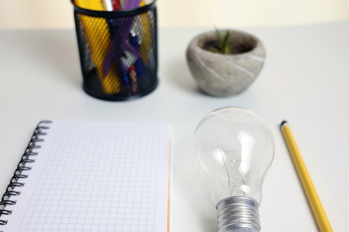 Un carnet, une ampoule, un crayon et une petite plante sur un bureau, symbolisant l'idéation environnementale