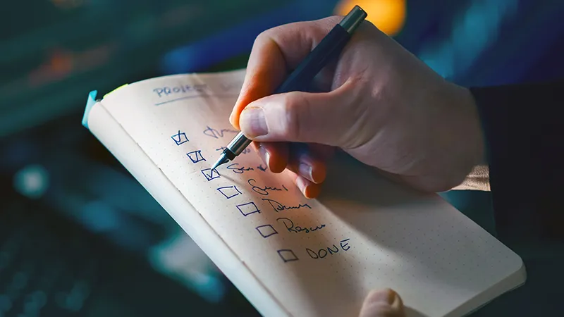 Main cochant des tâches sur une to-do list de gestion du temps, symbolisant l'efficacité en période de charge