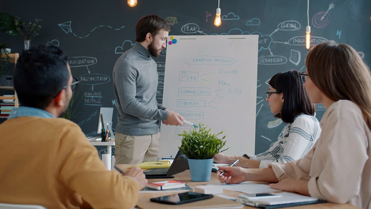 Équipe collaborant devant un tableau blanc pour expliquer une stratégie