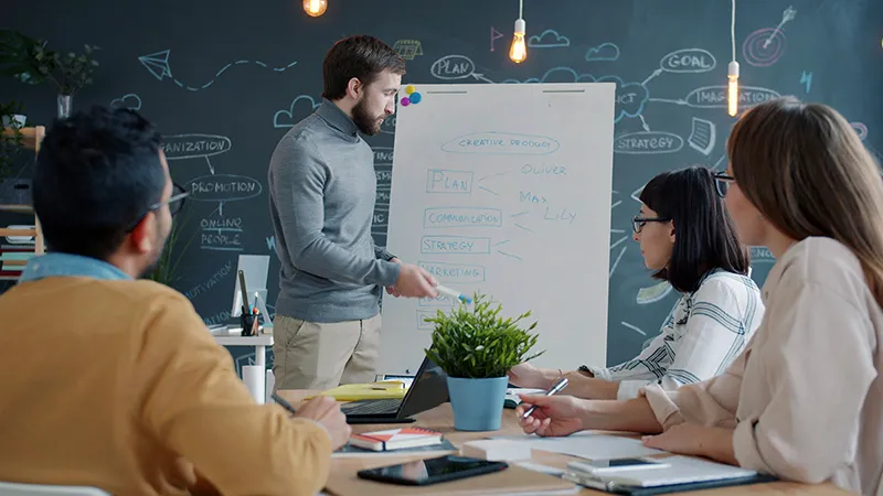 Équipe collaborant devant un tableau blanc pour expliquer une stratégie