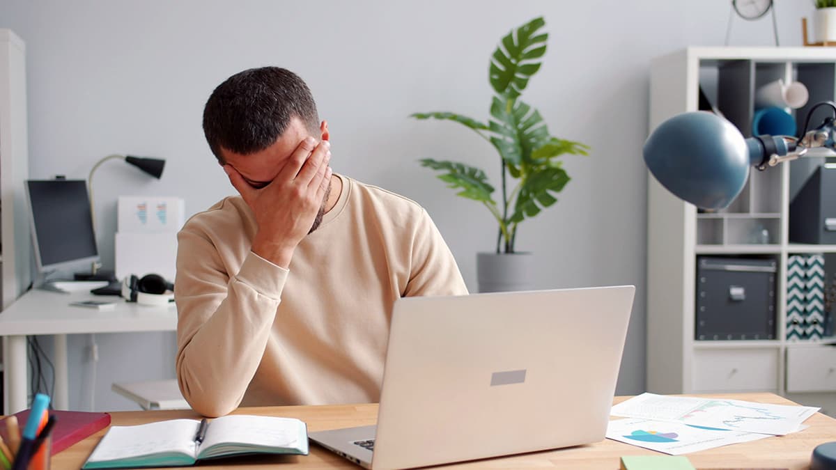 Une personne au bureau, le visage dans les mains, visiblement stressée et accablée devant son ordinateur