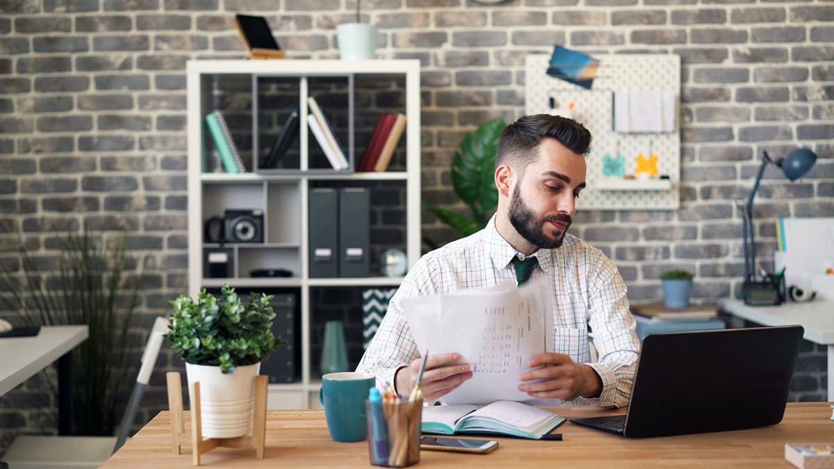 Un homme d'affaires pensif à son bureau, analysant un document avec recul, symbolisant l'apprentissage par l'échec